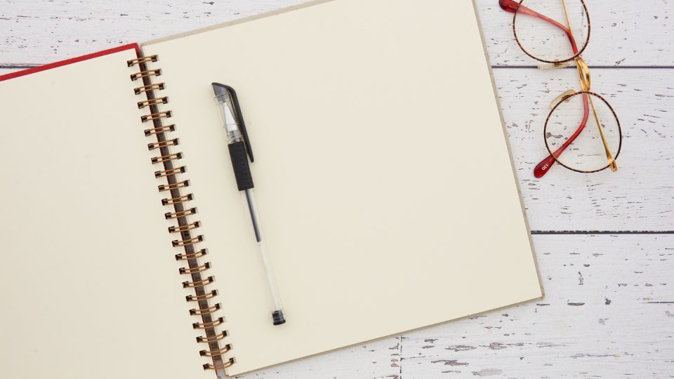 Carnet ouvert, stylo et lunettes sur une table claire
