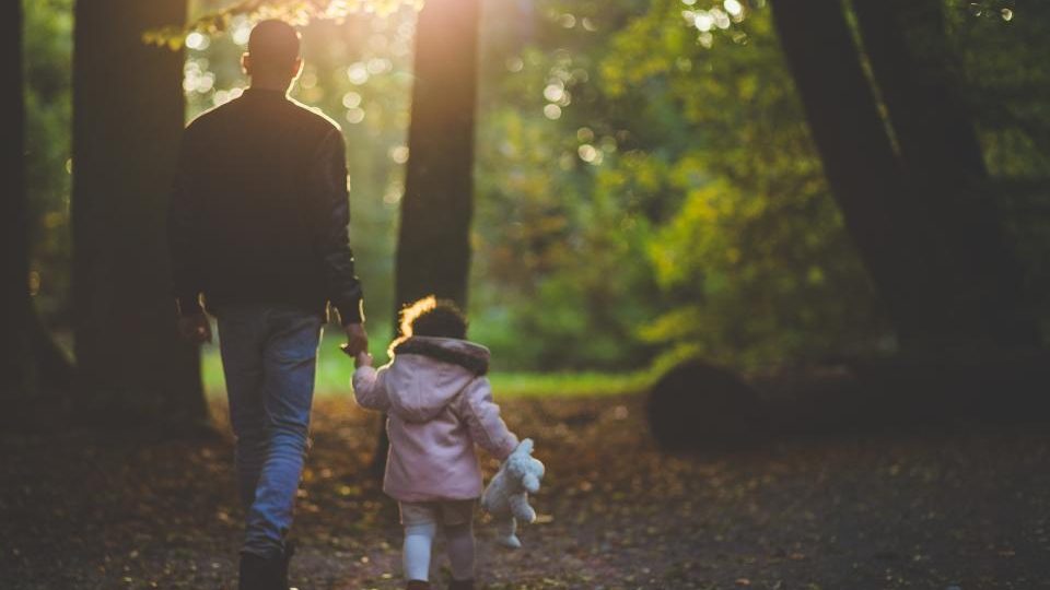Un père et sa fille marchent main dans la main sur un chemin boisé